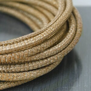 May include: A close-up of a roll of beige faux leather cord with a textured surface. The cord is woven in a tight pattern and is ideal for crafting projects.
