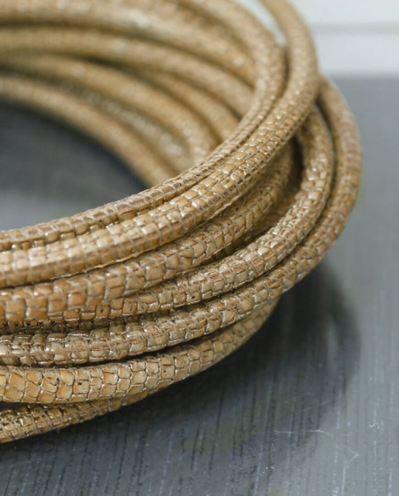 May include: A close-up of a roll of beige faux leather cord with a textured surface. The cord is woven in a tight pattern and is ideal for crafting projects.