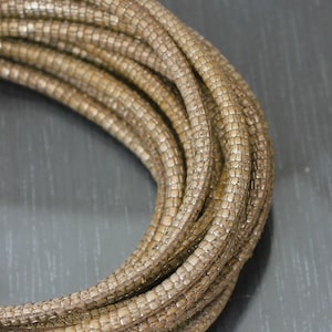 May include: A close-up of a beige braided cord, showing the intricate woven pattern. The cord is made of multiple strands of thin, flexible material, creating a textured and durable look.