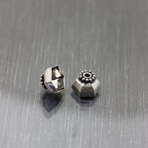 K&ouml;nnte beinhalten: Zwei silberne Metallperlen mit einem dekorativen Design. Die Perlen sind sechseckig und haben einen kleinen Kreis in der Mitte.