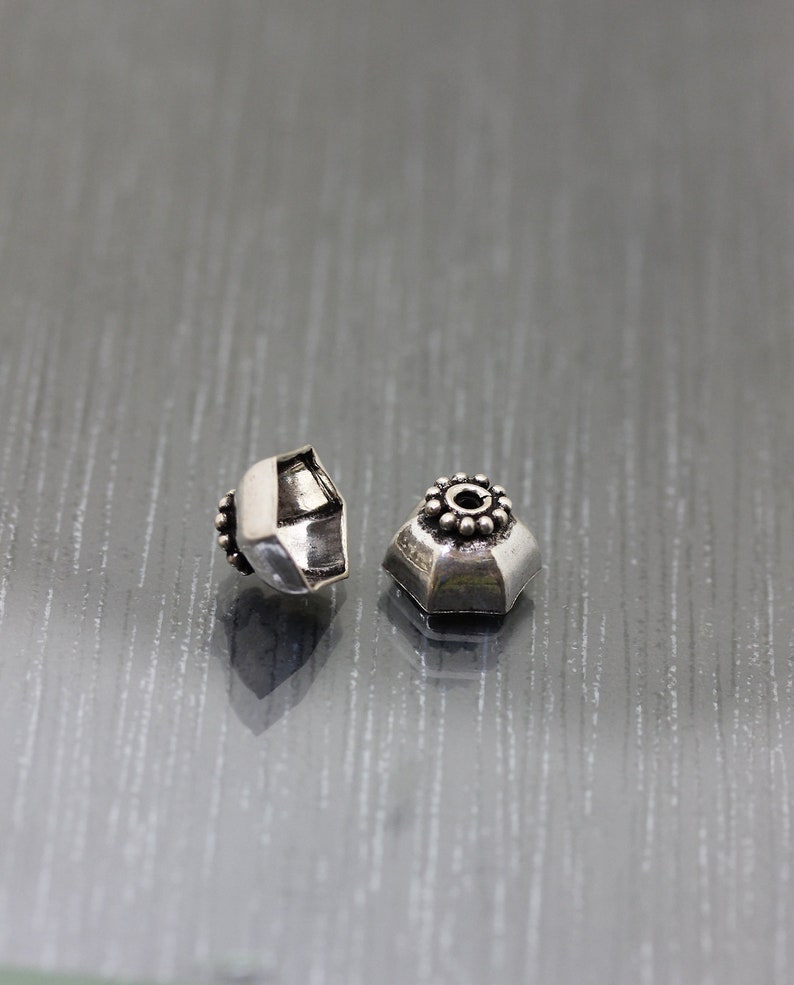K&ouml;nnte beinhalten: Zwei silberne Metallperlen mit einem dekorativen Design. Die Perlen sind sechseckig und haben einen kleinen Kreis in der Mitte.