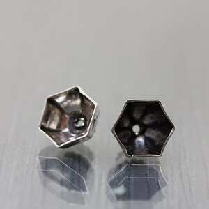 K&ouml;nnte beinhalten: Zwei sechseckige Ohrring-Findings aus silberfarbenem Metall mit einem kleinen Loch in der Mitte.
