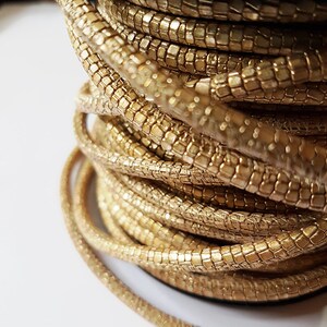 May include: A spool of gold-colored cord with a textured, scaly surface. The cord is wound tightly around the spool.