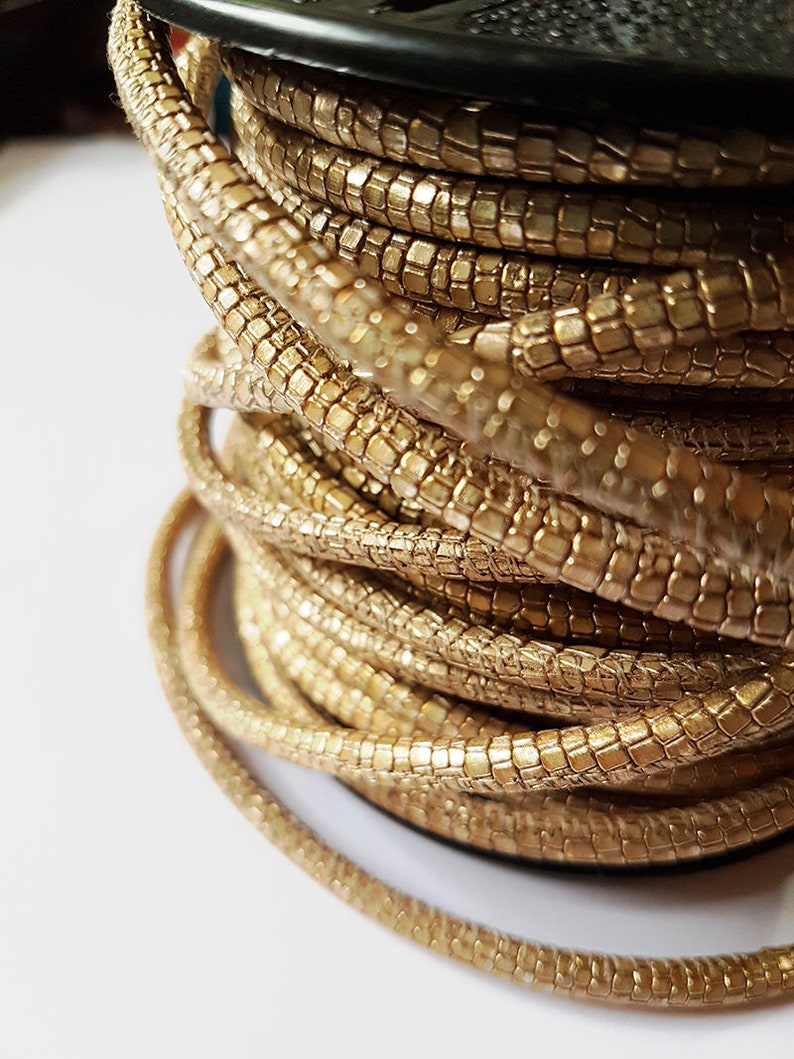 May include: A spool of gold-colored cord with a textured, scaly surface. The cord is wound tightly around the spool.