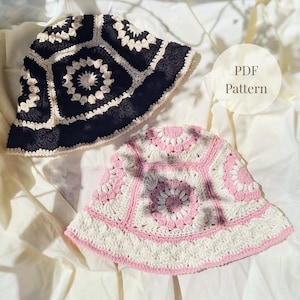 May include: Two crochet bucket hats. One is black and cream, the other is pink and white. The hats have a geometric design with a floral pattern in the center. The image includes the text "PDF Pattern".
