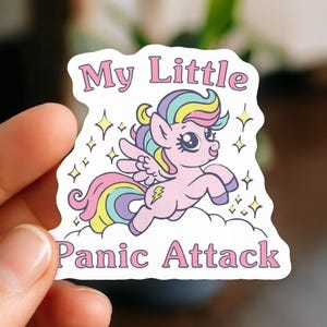 May include: A die-cut sticker featuring a light pink cartoon pony with a rainbow-colored mane and tail, wings, and a yellow lightning bolt symbol on its flank. The pony is above a white cloud with the text My Little Panic Attack in pink letters.