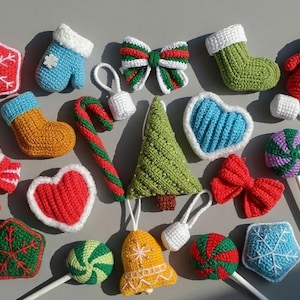 Könnte beinhalten: Eine Sammlung gehäkelter Weihnachtsanhänger, darunter rote und blaue Schneeflocken, Socken, Fäustlinge, Schleifen, eine Zuckerstange, ein grüner Baum, Herzen, eine Glocke und Lollis, alle mit detaillierten Garnstrukturen gefertigt.