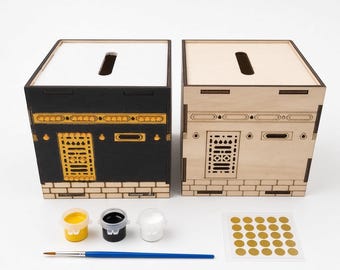 Puede incluir: Dos cajas cuadradas de madera con forma de Kaaba, una pintada de negro con detalles dorados y otra en madera clara natural. Incluye tres botes de pintura pequeños en amarillo, negro y blanco, un pincel azul y una hoja de veinticinco pegatinas doradas.