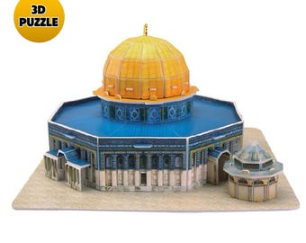 Puede incluir: Un rompecabezas 3D de la Cúpula de la Roca que presenta una cúpula dorada prominente, un techo octogonal azul y patrones de azulejos azules y blancos intrincados en las paredes. Una estructura secundaria más pequeña se sitúa a la derecha sobre una base de color tostado claro.