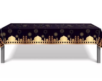 Puede incluir: Un mantel rectangular negro con un diseño dorado de mezquita y fuegos artificiales. El mantel está colocado sobre una mesa con patas plateadas. El diseño presenta cúpulas y minaretes dorados, creando un aspecto festivo.