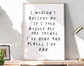 Puede incluir: Un cuadro enmarcado con la cita "I wouldn't believe me if I told myself all the things I've done and places I've run." El texto negro está escrito a mano sobre un fondo blanco. El marco es de madera clara. El cuadro está sobre un escritorio.