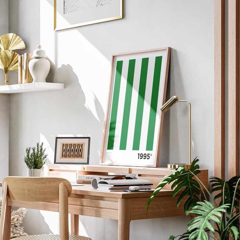 Puede incluir: Un cuadro enmarcado con rayas verticales verdes y el a&ntilde;o "1995" en blanco. La obra de arte se exhibe en un escritorio de madera con una l&aacute;mpara de escritorio dorada. Otros elementos decorativos est&aacute;n presentes.