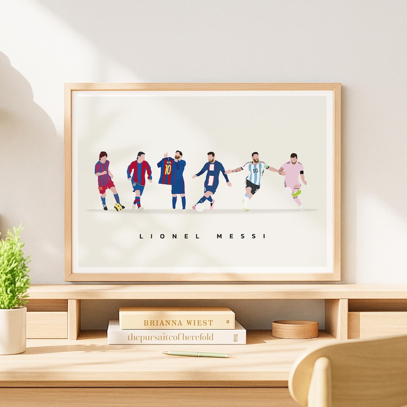 May include: A framed print featuring a stylized illustration of Lionel Messi in various soccer uniforms. The artwork showcases Messi in different team jerseys, with the name "Lionel Messi" printed below in black letters. The print is displayed on a wooden desk.
