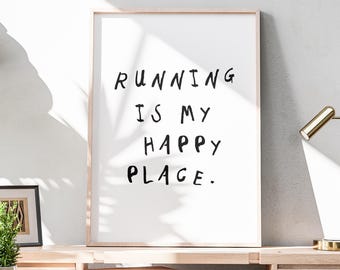 May include: A framed print with the text "RUNNING IS MY HAPPY PLACE" in black lettering. The print has a light wood frame and is displayed on a wooden desk. A small framed picture and a potted plant are also on the desk.
