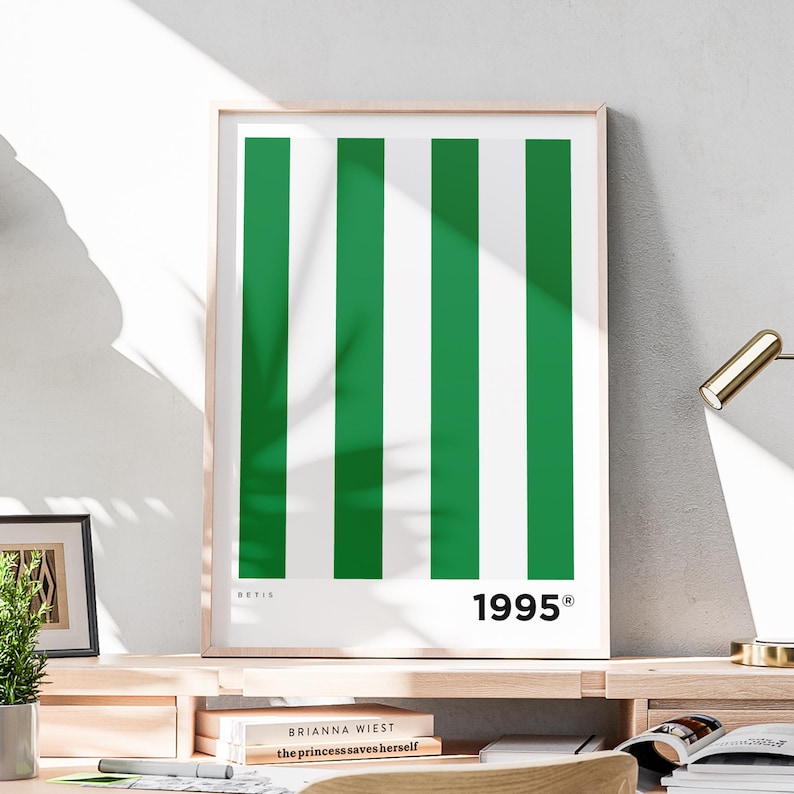 Puede incluir: Un estampado enmarcado con un dise&ntilde;o de rayas verticales verdes y blancas alternas. La palabra "BETIS" est&aacute; impresa en la parte superior izquierda y el n&uacute;mero "1995" en la parte inferior derecha. El estampado se muestra sobre una superficie de madera.