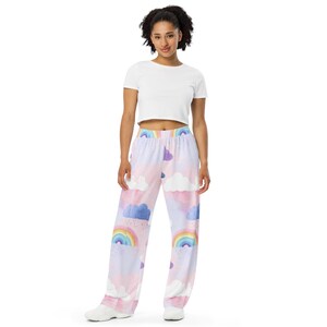 May include: A person wearing a white crop top and pajama pants. The pajama pants feature a watercolor design of rainbows, clouds, and rain in shades of pink, purple, blue, and yellow. The pants have a wide-leg design.