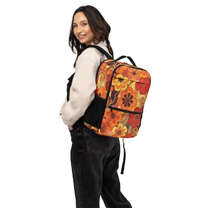 May include: A backpack with a vibrant floral pattern in shades of orange, yellow, and red. The backpack has black side pockets and straps. The design features a retro flower power aesthetic.