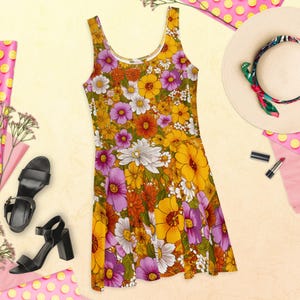 May include: A sleeveless skater dress with a vibrant floral pattern in shades of yellow, orange, purple, and white. The dress is paired with black heeled sandals and a straw hat with a colorful scarf. Lipstick and a pink polka dot background complete the look.