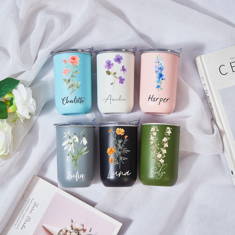 May include: Six stainless steel tumblers in various colors, each with a floral design and a name. Colors include light blue, white, pink, gray, black, and green. The names are Charlotte, Amelia, Harper, Sofia, Luna, and Evelyn. Each tumbler has a silver lid.