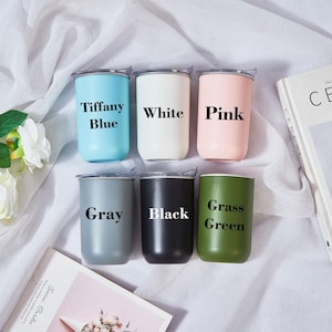 May include: Six insulated tumblers in various colors: Tiffany Blue, White, Pink, Gray, Black, and Grass Green. Each tumbler has a silver lid and the color name printed on the front. A book and flowers are in the background.