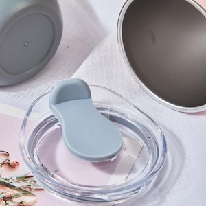 May include: Close-up of several insulated tumblers and lids. One tumbler is pink, another is gray, and a third is white. The clear lid has a light blue slider. The tumblers are on a white cloth.