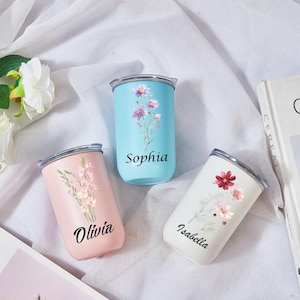 May include: Three insulated tumblers in pastel colors: light blue, pink, and white. Each tumbler features a floral design and a name: Sophia, Olivia, and Isabella. The tumblers have silver lids and are set against a white background.