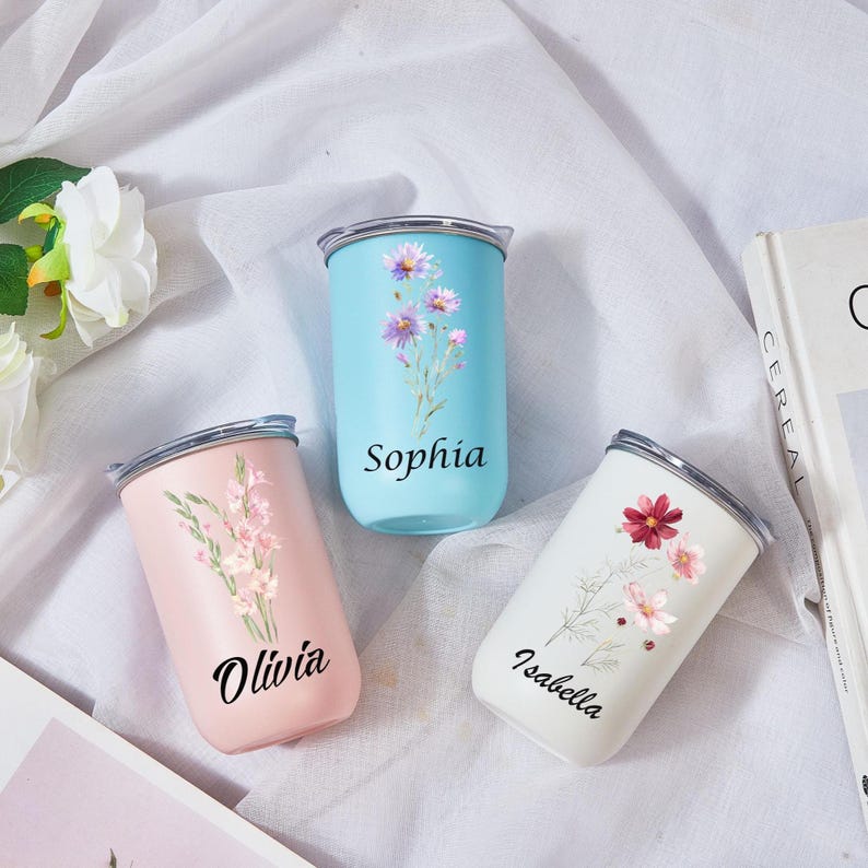 May include: Three insulated tumblers in pastel colors: light blue, pink, and white. Each tumbler features a floral design and a name: Sophia, Olivia, and Isabella. The tumblers have silver lids and are set against a white background.