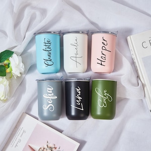 以下が含まれることがあります： ライトブルー、白、ピンク、グレー、黒、オリーブグリーンの6色のパーソナライズされたタンブラー。各タンブラーには、Charlotte、Amelia、Harper、Sofia、Luna、Evelynという異なる名前がエレガントな筆記体で書かれています。タンブラーには透明な蓋が付いています。