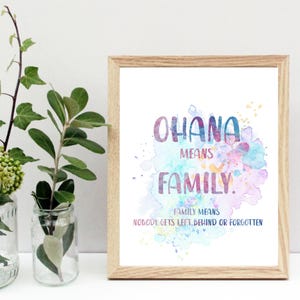 Peut inclure: Une affiche encadr&eacute;e avec les mots "OHANA MEANS FAMILY" en lettrage aquarelle color&eacute;. L'affiche est dans un cadre en bois clair et pr&eacute;sente un fond &eacute;clabouss&eacute; d'aquarelle. Deux bocaux en verre avec de la verdure sont devant l'affiche.