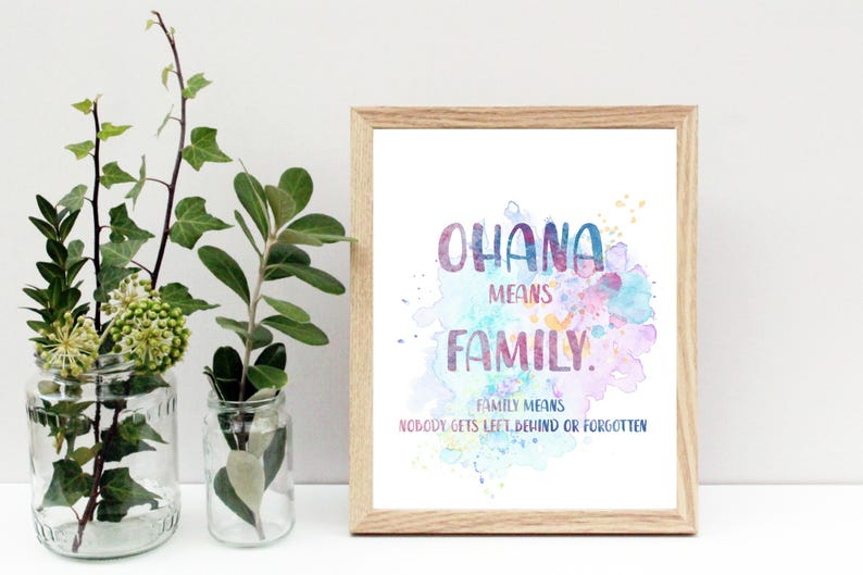 Peut inclure: Une affiche encadr&eacute;e avec les mots "OHANA MEANS FAMILY" en lettrage aquarelle color&eacute;. L'affiche est dans un cadre en bois clair et pr&eacute;sente un fond &eacute;clabouss&eacute; d'aquarelle. Deux bocaux en verre avec de la verdure sont devant l'affiche.
