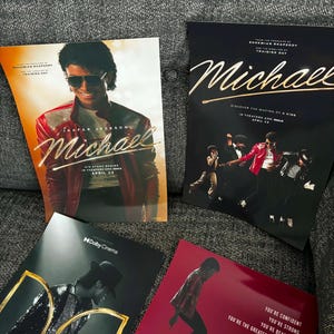 May include: Four promotional posters for the movie "Michael" featuring images of Michael Jackson. The posters have a red, black, and gold color scheme. The text on the posters includes "Michael" and "Discover the Making of a King".