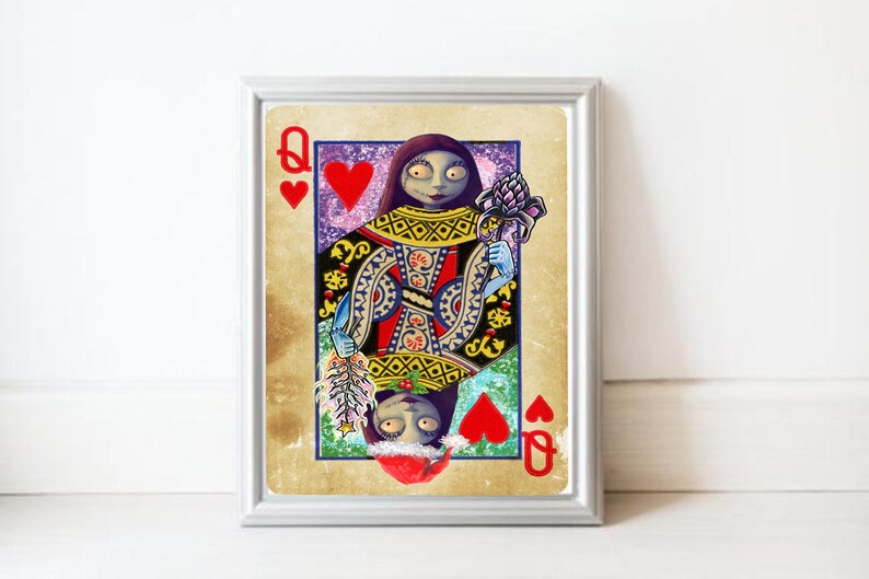 May include: Framed art print featuring a stylized Queen of Hearts card. The artwork depicts a character with pale skin, dark hair, and blue arms, holding a flower and a feather. The card has a vintage, distressed look with red hearts.