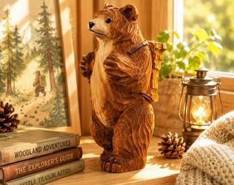May include: A brown bear figurine standing on its hind legs, featuring carved wood-like textures and a backpack on its back. The bear has a lighter-colored chest and snout, with a dark nose and eyes, captured in a standing pose with front paws raised.