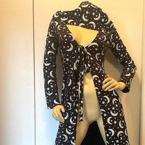 Op de afbeelding: Een lange zwarte robe met een zilveren halve maan en sterrenpatroon. De robe heeft een strik in de taille en een diepe V-hals.