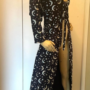 Op de afbeelding: Een lange zwarte robe met een zilveren halve maan en sterrenpatroon. De robe heeft een strik in de taille en een lange, vloeiende rok.