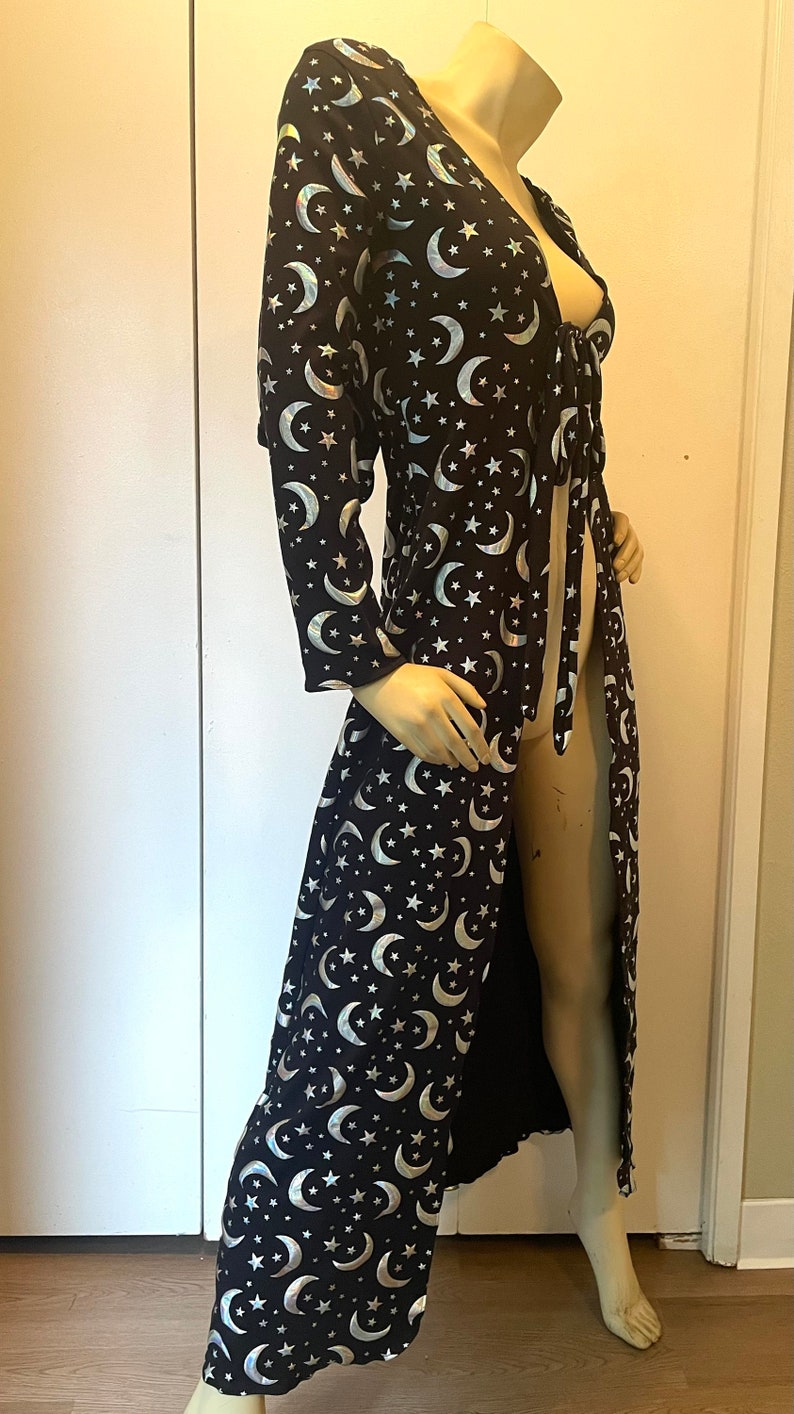 Op de afbeelding: Een lange zwarte robe met een zilveren halve maan en sterrenpatroon. De robe heeft een strik in de taille en een lange, vloeiende rok.