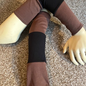 May include: A pair of brown and black arm warmers with a striped design. The arm warmers are made of a soft, stretchy fabric.