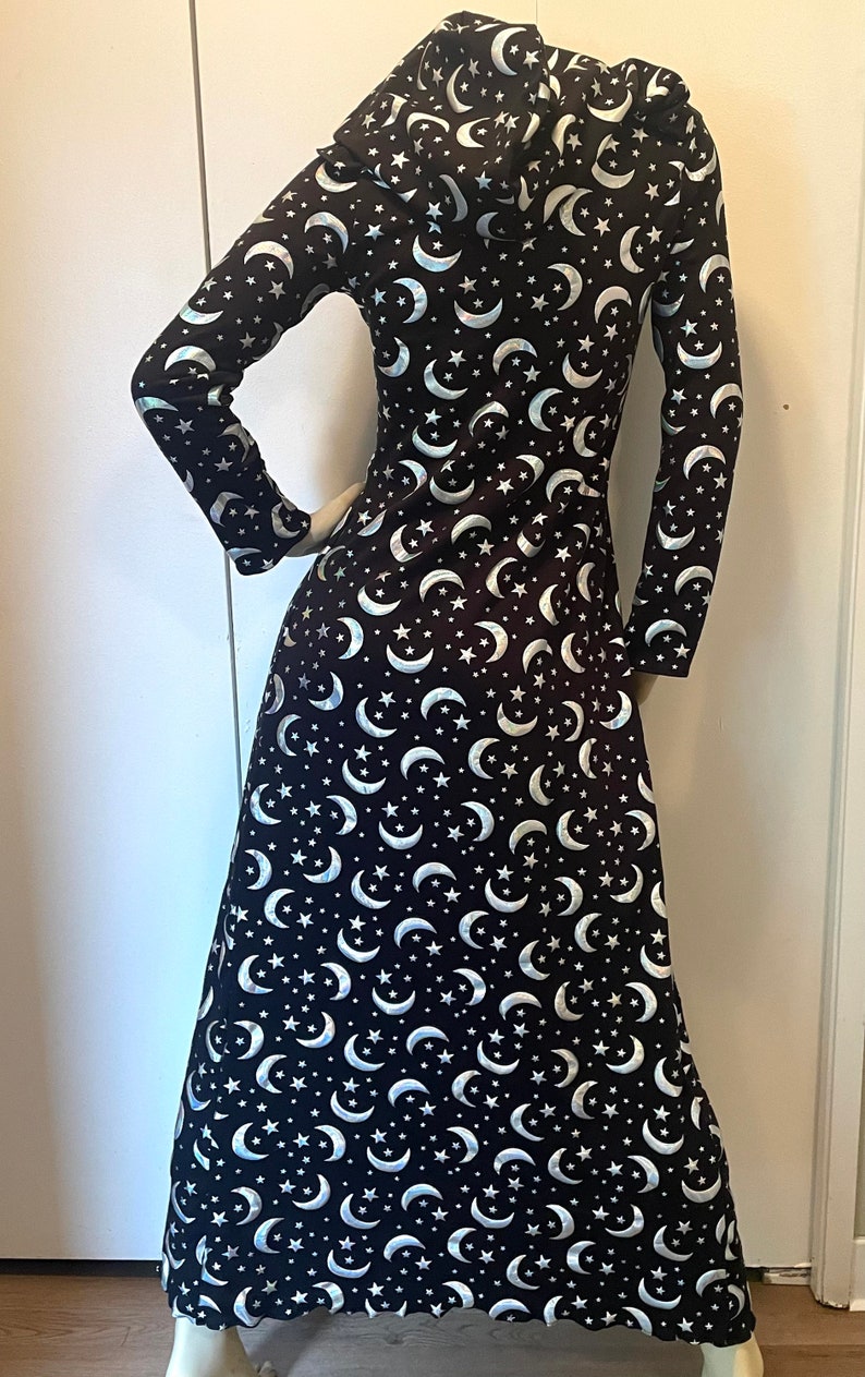 Op de afbeelding: Een lange zwarte gekapte robe met een zilveren halve maan en sterrenpatroon. De robe heeft lange mouwen en een zwierige rok.