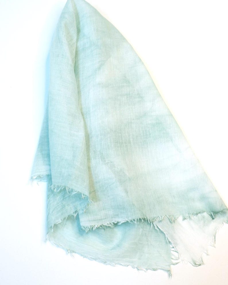 May include: A light blue, sheer fabric scarf with a frayed edge. The fabric has a subtle, uneven texture.