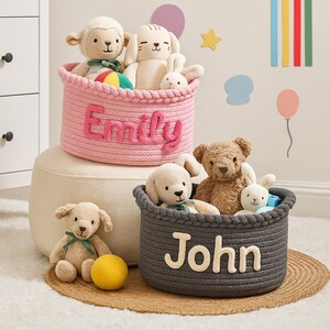 Puede incluir: Dos cestas de cuerda, una rosa con "Emily" y otra gris con "John", llenas de peluches. Un puf beige est&aacute; debajo de la cesta rosa. Un perro de peluche y una pelota amarilla est&aacute;n delante. Decoraciones de pared en el fondo.
