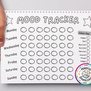 May include: A spiral-bound mood tracker with the words "MOOD TRACKER" at the top. The days of the week are listed down the left side, with circles for tracking moods. A color key lists emotions like happy, sad, and worried. The image is held by two hands.