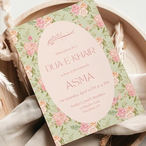 以下が含まれることがあります： 柔らかいピンクの楕円の中に「DUA-E-KHAIR」と「ASMA」の文字が入ったフローラル招待状。カードは、ピンクとピーチのバラが入った薄緑色の背景です。招待状は、乾燥した植物とベージュの布が入った木製のトレイに置かれています。