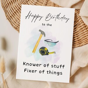 Könnte beinhalten: Eine weiße Geburtstagskarte mit dem Text "Happy Birthday to the Knower of stuff Fixer of things". Die Karte zeigt Aquarellillustrationen eines Hammers, einer Schutzbrille und eines Maßbands.