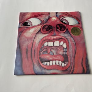 May include: A red and blue album cover with a close-up image of a face with a large open mouth and a tongue sticking out. The face is painted in a watercolor style and has a gold sticker on the right side that reads 'Limited Edition Remastered'. 
