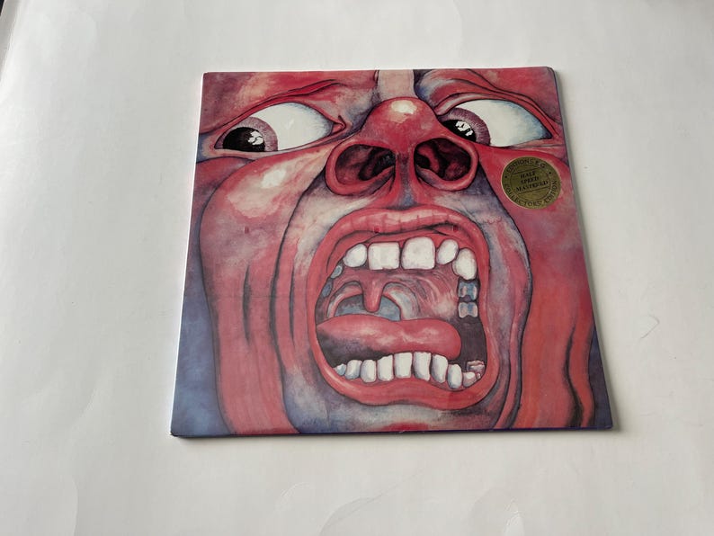 May include: A red and blue album cover with a close-up image of a face with a large open mouth and a tongue sticking out. The face is painted in a watercolor style and has a gold sticker on the right side that reads 'Limited Edition Remastered'. 