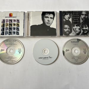 May include: Three compact discs and three CD cases. The CD cases are silver with black text. The CDs are silver with black text. The text on the CD cases reads "Jeff Beck Group Rough and Ready" and "Peter Gabriel So".