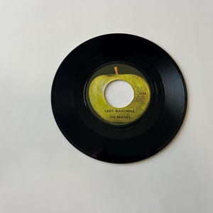 May include: A black vinyl record with a green apple label. The label features the text "Lady Madonna" and "The Beatles".