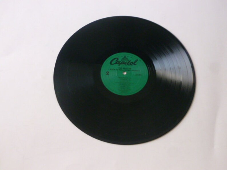 Op de afbeelding: Zwarte vinylplaat met een groen label waarop "Capitol" en "The Miracles" staat met een lijst van nummers. De plaat ligt op een wit oppervlak.