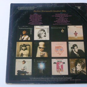 May include: A black and white vinyl record album cover featuring a collage of photos of a woman with different hairstyles and outfits. The album title is "Barbra Streisand's Greatest Hits" and the album cover includes the text "Side 1" and "Side 2".