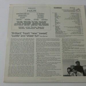 May include: A vintage record album cover for the musical "Hair" featuring a cast photo of the actors. The album cover is white with black text and a photo of the cast in the bottom right corner. The text on the cover reads "Hair" and "Michael Butler".